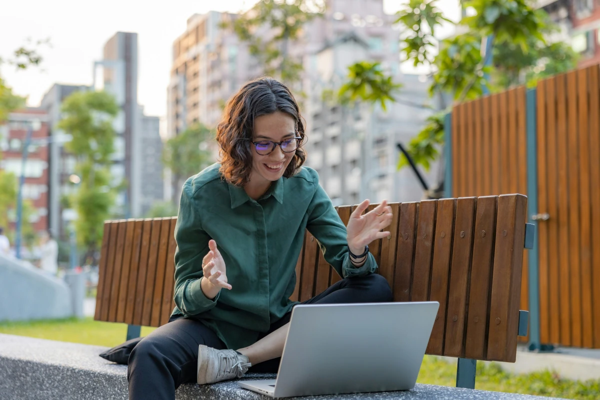 Young adult sitting outside talking to a laptop during a virtual therapy session
